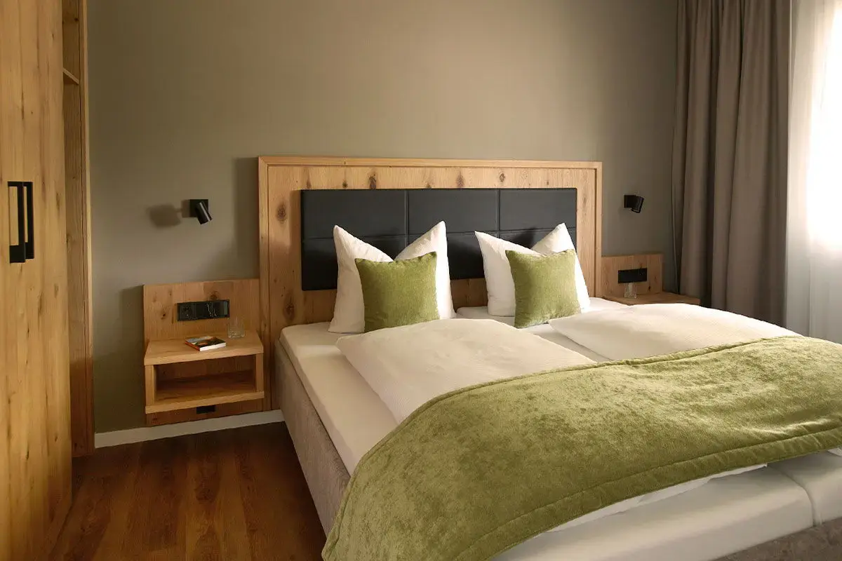 Blick in den Schlafraum der Komfortsuite Deluxe - mit viel Holz, natürlichen Farben und freundlich grüner Kissendeko