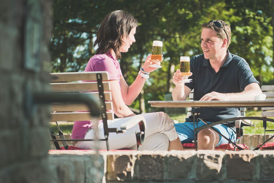 Paar sitzt im Biergarten der Dorfschänke und stößt mit einem Bier an