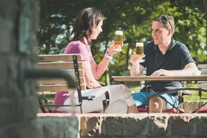 Ein Pärchen sitzt im Biergarten am Tisch und stößt auf das schönes Wetter an.