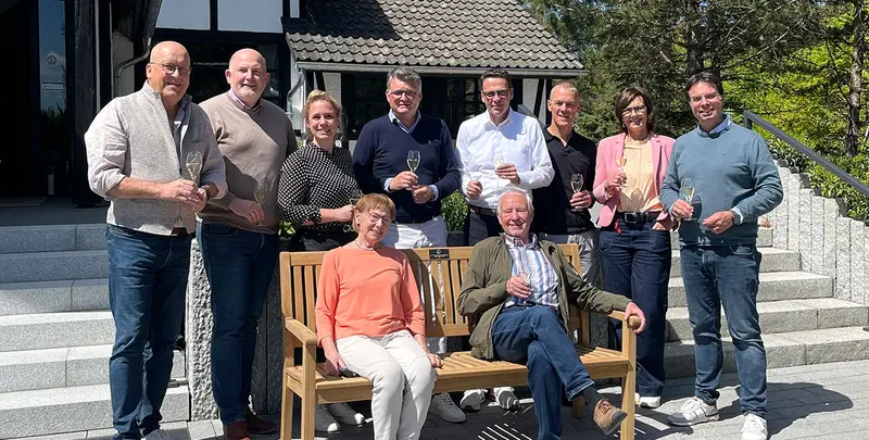 Gruppenbild mit Personen um gespendeter Parkbank vor dem Eingang des Hotels