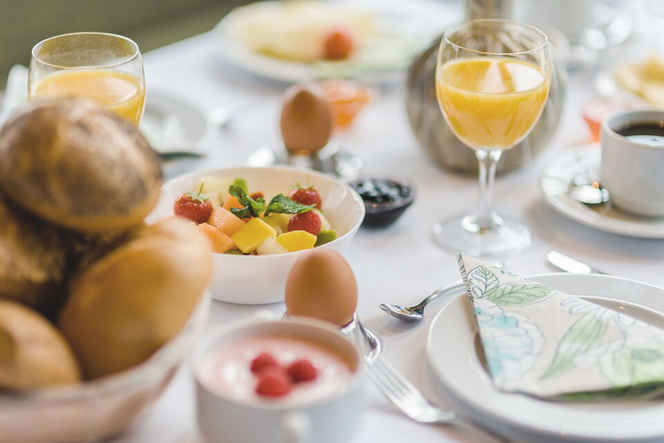 Blick auf einen gedeckten Tisch mit frischem Frühstück, bestehend aus Brötchen, Jogurt, Kaffee, Ost, Ei und vielem mehr