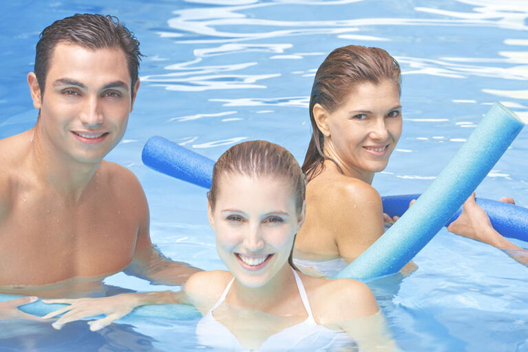 Personen schwimmen im Hallenbad des Sporthotel Grafenwald und lächeln in die Kamera