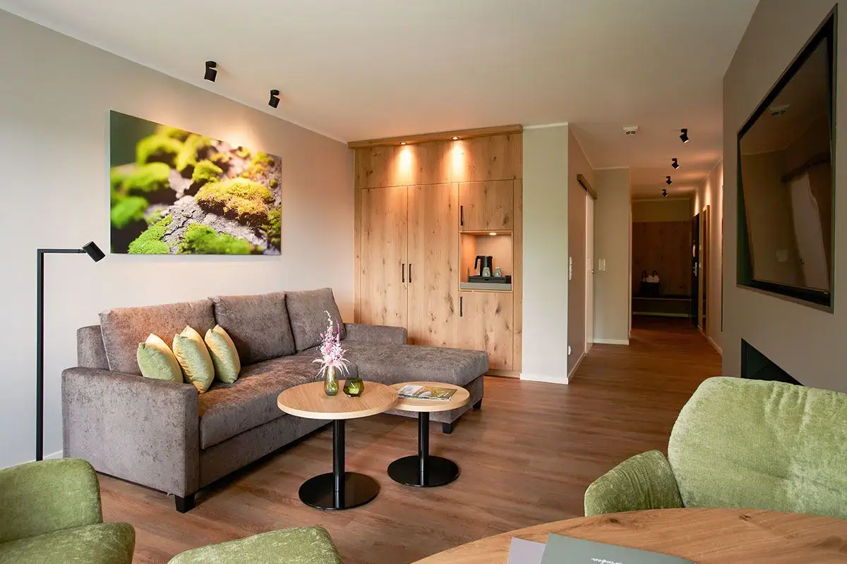 Wohnzimmer der Kofortsuite Deluxe - mit Ecksofa, großem Flatscreen, grünen Coctailsesseln, viel Holz und schöner Beleuchtung
