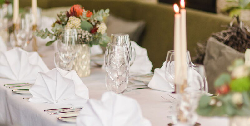 Detailaufnahme gedeckter Tisch mit Gläsern, Servietten, Blumen und Kerzen im Restaurant Grafenwald