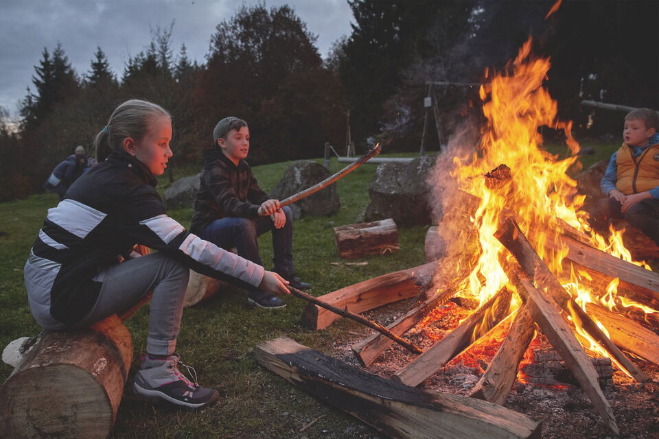 Kids Club Veranstaltung: Kinder sitzen bei Abendstimmung am Lagerfeuer und machen Stockbrot